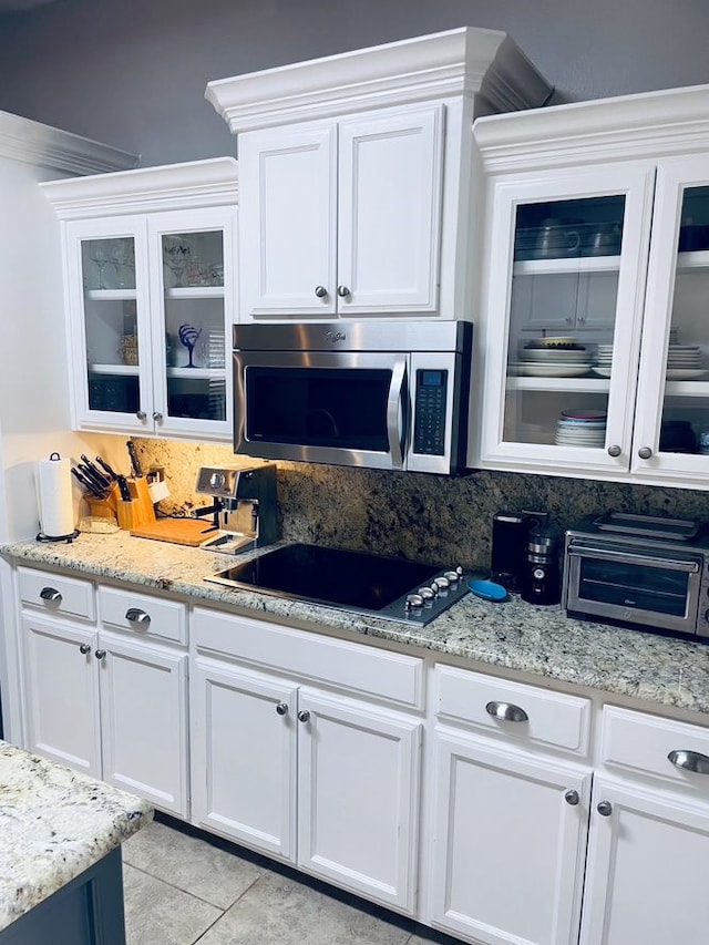 kitchen featuring tasteful backsplash, stainless steel microwave, white cabinetry, and black electric cooktop