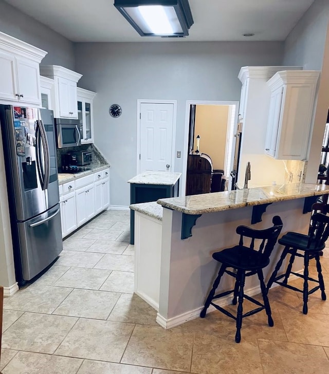 kitchen with a peninsula, white cabinetry, appliances with stainless steel finishes, a center island, and tasteful backsplash