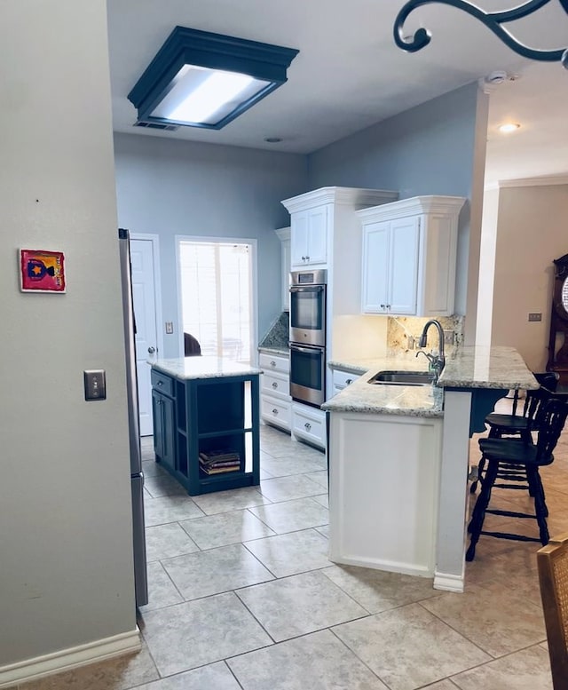 kitchen featuring white cabinets, a sink, light stone countertops, double oven, and backsplash