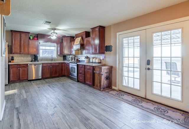 kitchen featuring french doors, custom exhaust hood, appliances with stainless steel finishes, light hardwood / wood-style floors, and decorative backsplash