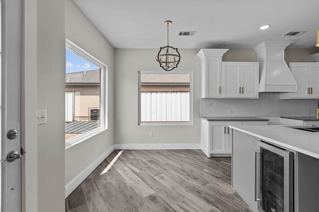 kitchen with an inviting chandelier, white cabinets, beverage cooler, and custom exhaust hood