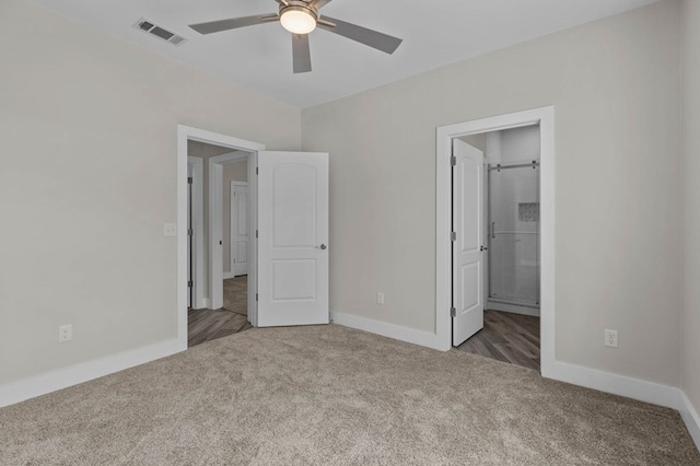 unfurnished bedroom featuring dark colored carpet, ensuite bathroom, and ceiling fan