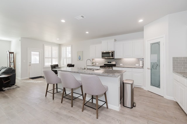 kitchen with light stone countertops, white cabinetry, stainless steel appliances, and a kitchen island with sink