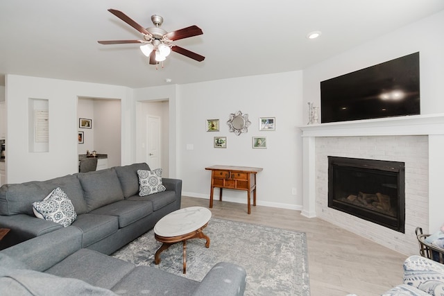 living room with light wood-type flooring, a brick fireplace, and ceiling fan