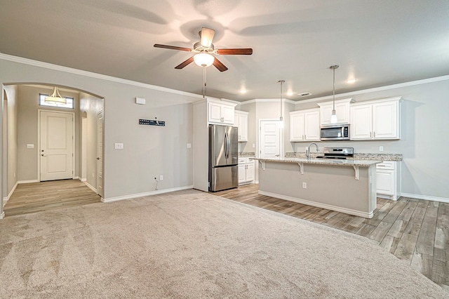 kitchen with a center island with sink, hanging light fixtures, appliances with stainless steel finishes, light stone counters, and white cabinetry