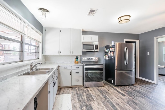 702 Dellwood St, Midland, TX 79701 - kitchen featuring stainless steel appliances, a sink, light wood-type flooring, backsplash, and white cabinetry