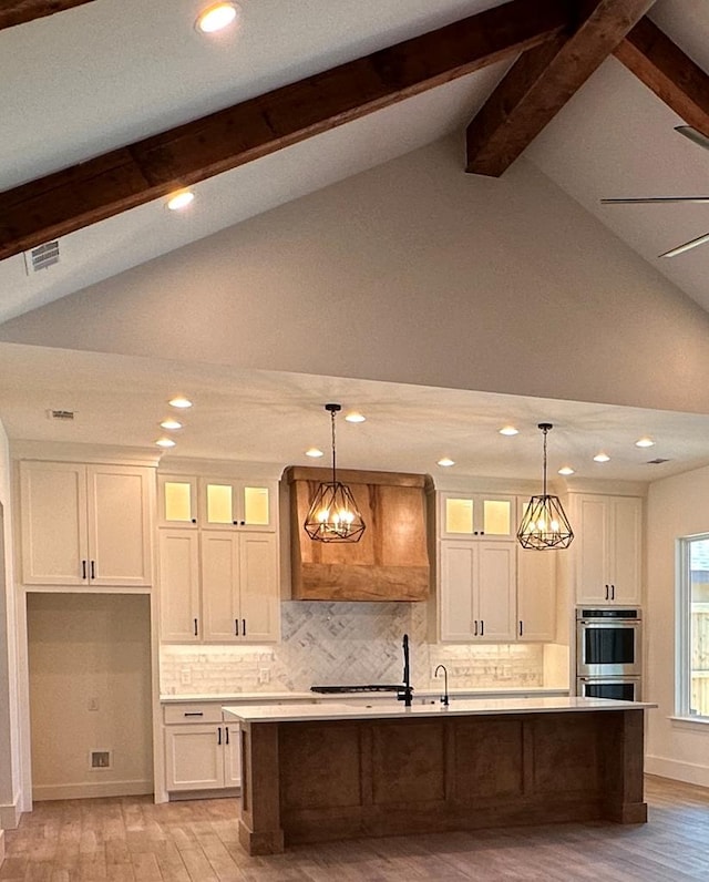 kitchen featuring pendant lighting, vaulted ceiling with beams, and a center island with sink