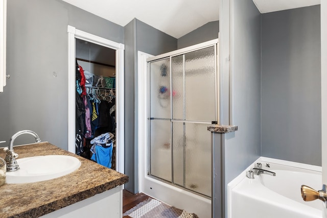 bathroom with a stall shower, vaulted ceiling, a walk in closet, vanity, and a bath