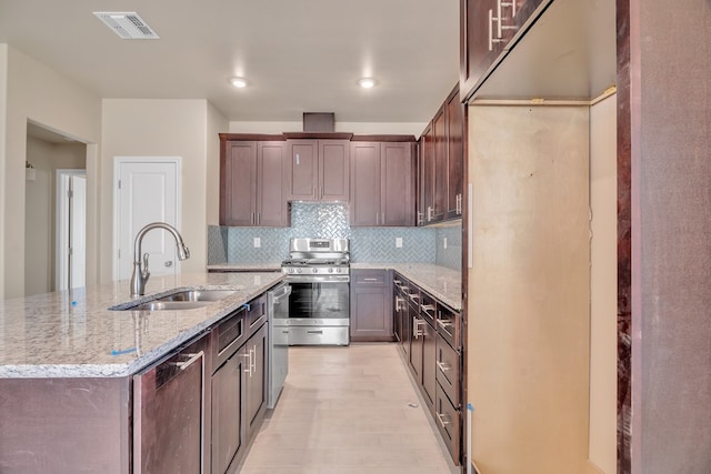 kitchen with sink, a kitchen island with sink, backsplash, dark brown cabinetry, and gas range