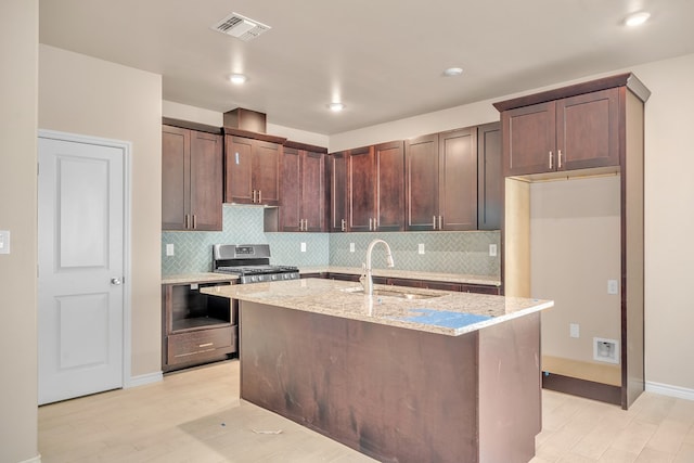 kitchen featuring sink, a kitchen island with sink, dark brown cabinetry, stainless steel range, and light stone countertops