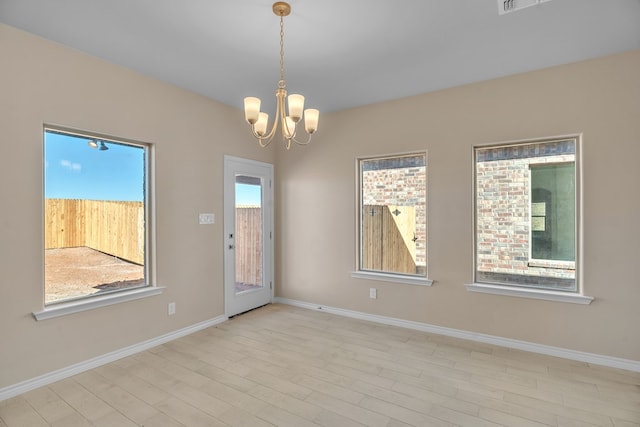 empty room featuring a healthy amount of sunlight, an inviting chandelier, and light hardwood / wood-style floors