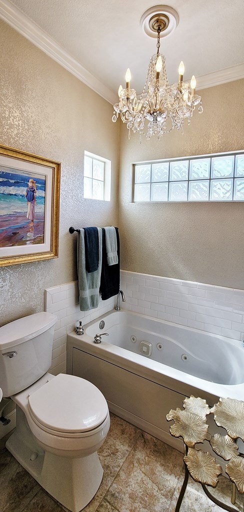 bathroom with toilet, an inviting chandelier, ornamental molding, and a tub