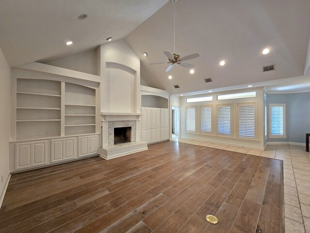 unfurnished living room with wood-type flooring, ceiling fan, high vaulted ceiling, a fireplace, and built in features