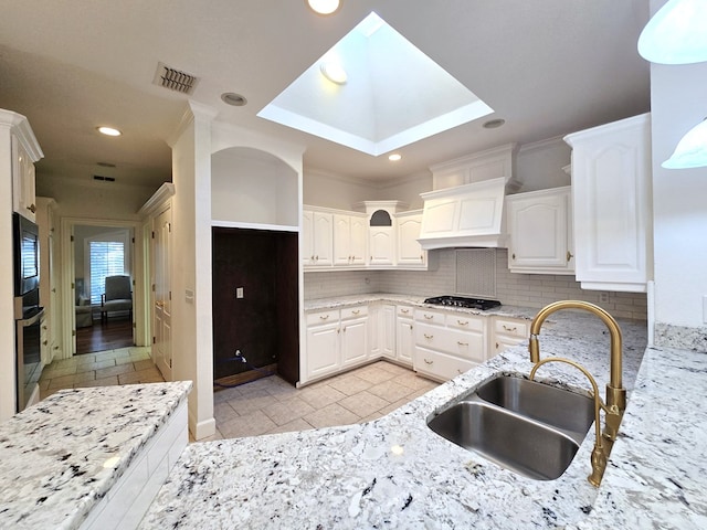 kitchen featuring custom exhaust hood, gas stovetop, sink, white cabinetry, and backsplash