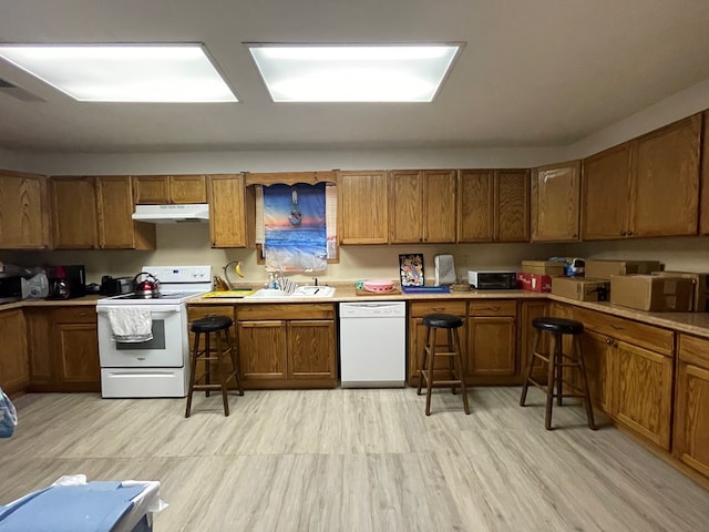 kitchen featuring under cabinet range hood, white appliances, a sink, visible vents, and brown cabinetry