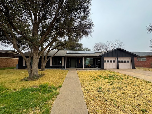 ranch-style home featuring a garage, a front yard, and solar panels