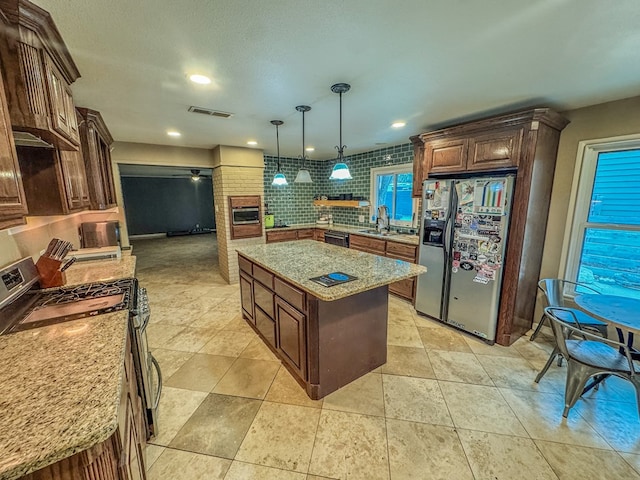 kitchen featuring sink, appliances with stainless steel finishes, a center island, light stone counters, and decorative light fixtures