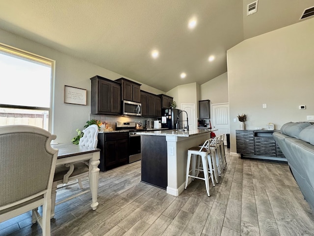 6005 Scaled Quail Rd, Midland, TX 79707 - kitchen featuring stainless steel appliances, an island with sink, light wood finished floors, open floor plan, and a breakfast bar