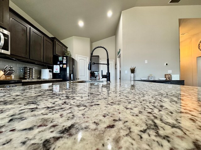 6005 Scaled Quail Rd, Midland, TX 79707 - kitchen with black fridge, light stone counters, tasteful backsplash, lofted ceiling, and stainless steel microwave
