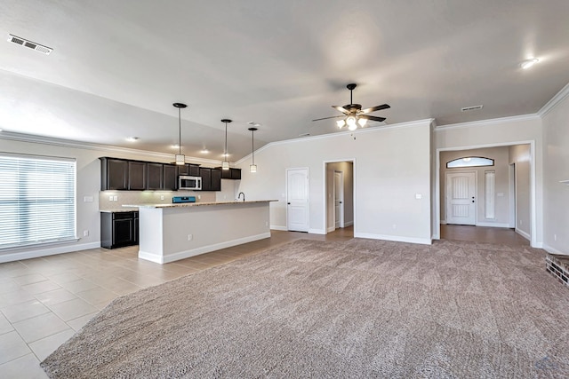 kitchen featuring ceiling fan, pendant lighting, light colored carpet, a center island with sink, and ornamental molding