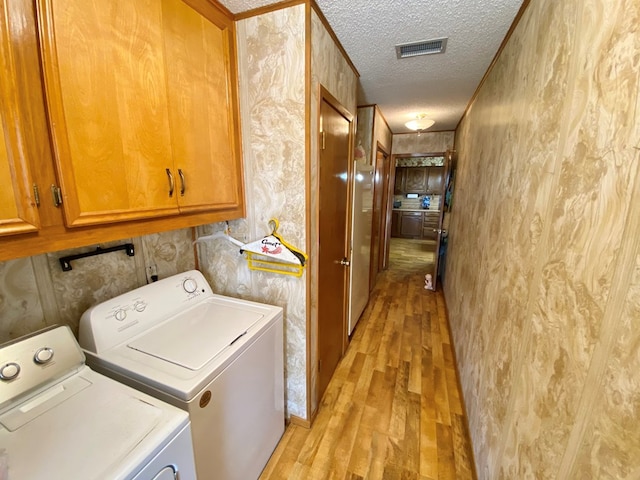 laundry area featuring cabinets, a textured ceiling, light hardwood / wood-style flooring, and washing machine and clothes dryer