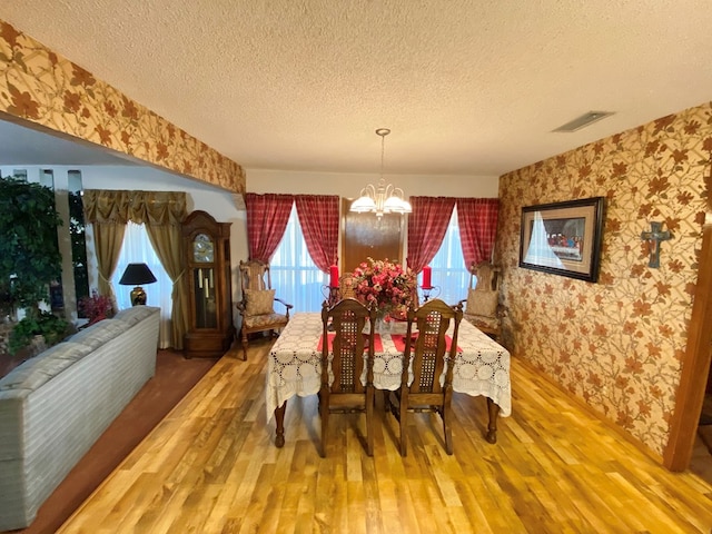 dining room featuring wood-type flooring, a textured ceiling, and an inviting chandelier