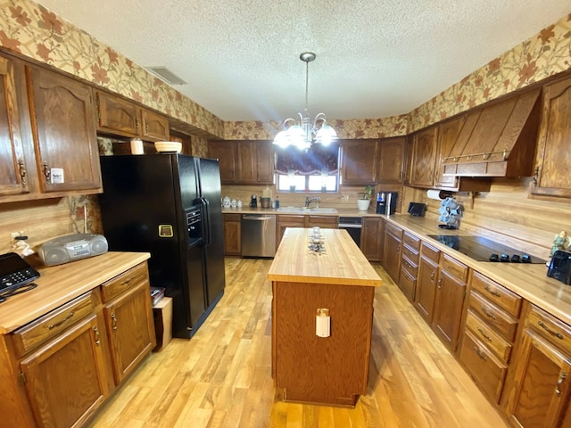 kitchen featuring black appliances, a notable chandelier, a center island, light hardwood / wood-style floors, and butcher block counters