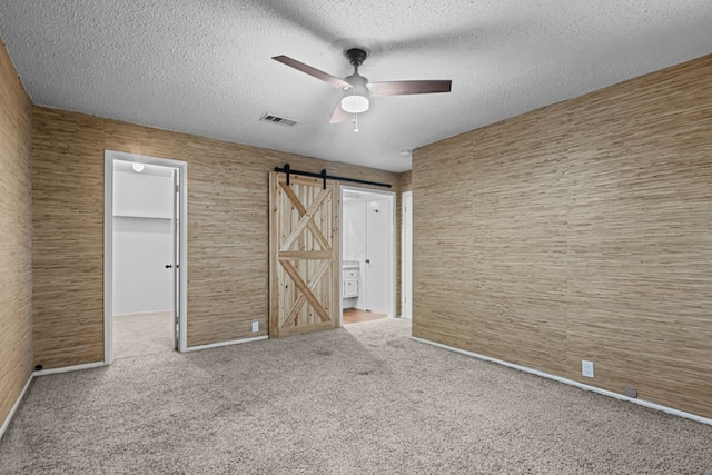 unfurnished bedroom with a barn door, carpet flooring, a textured ceiling, and a spacious closet