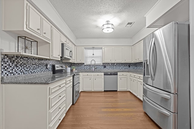 kitchen with sink, light hardwood / wood-style flooring, dark stone countertops, appliances with stainless steel finishes, and white cabinets