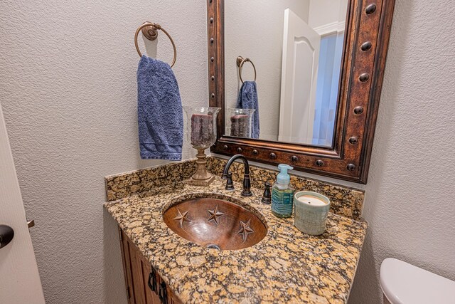 half bathroom featuring toilet, a textured wall, and vanity