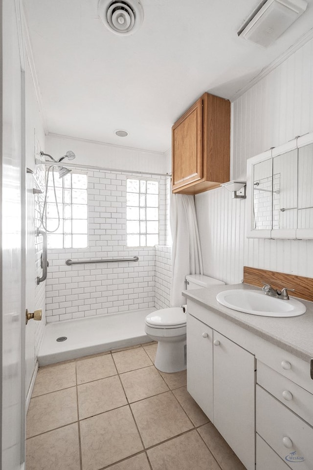 bathroom featuring toilet, a tile shower, tile patterned flooring, ornamental molding, and vanity