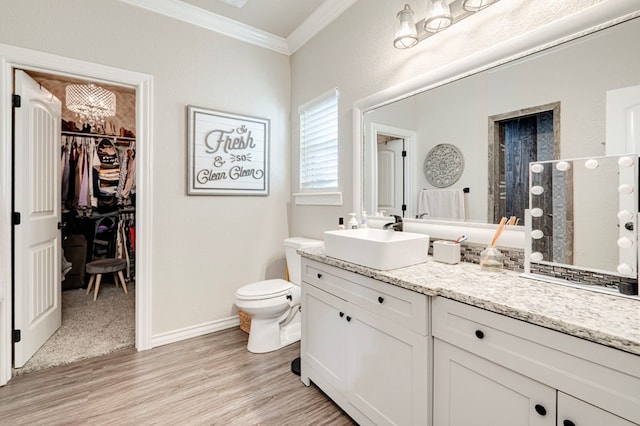 bathroom featuring crown molding, vanity, wood finished floors, toilet, and a spacious closet