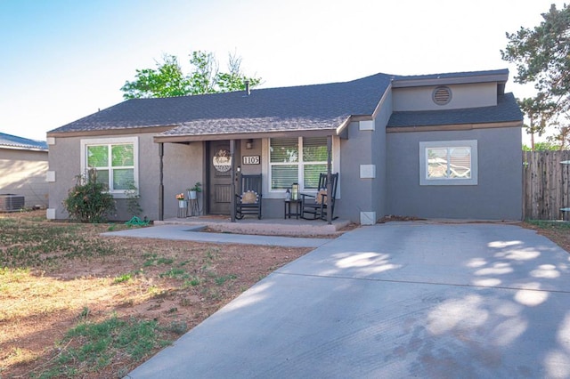 single story home featuring covered porch, roof with shingles, central AC, fence, and stucco siding