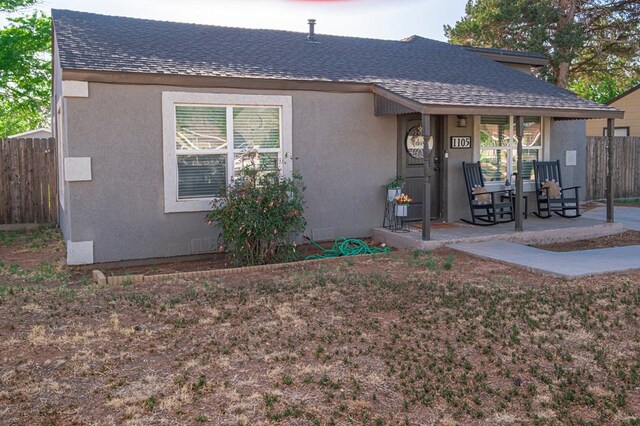 view of front of home with stucco siding, a shingled roof, and fence