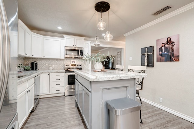 kitchen featuring backsplash, visible vents, crown molding, appliances with stainless steel finishes, and a breakfast bar
