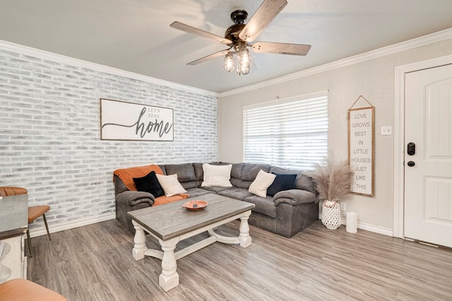 living room featuring a ceiling fan, brick wall, baseboards, light wood finished floors, and ornamental molding