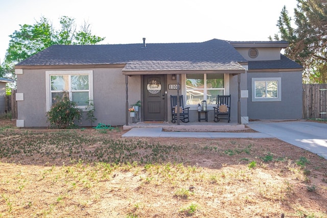 single story home featuring covered porch, fence, roof with shingles, and stucco siding