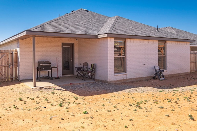 rear view of house with brick siding, fence, a shingled roof, and a patio