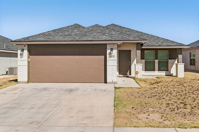 prairie-style home featuring a garage, central air condition unit, brick siding, concrete driveway, and a shingled roof