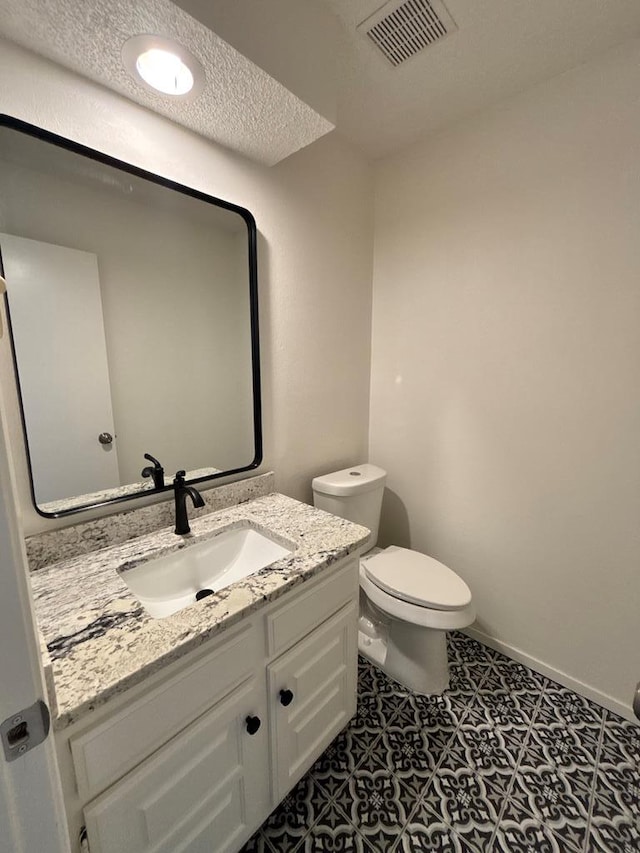 half bathroom with visible vents, toilet, a textured ceiling, baseboards, and vanity