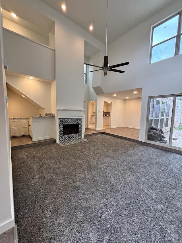 unfurnished living room featuring a towering ceiling, carpet, a wealth of natural light, and ceiling fan