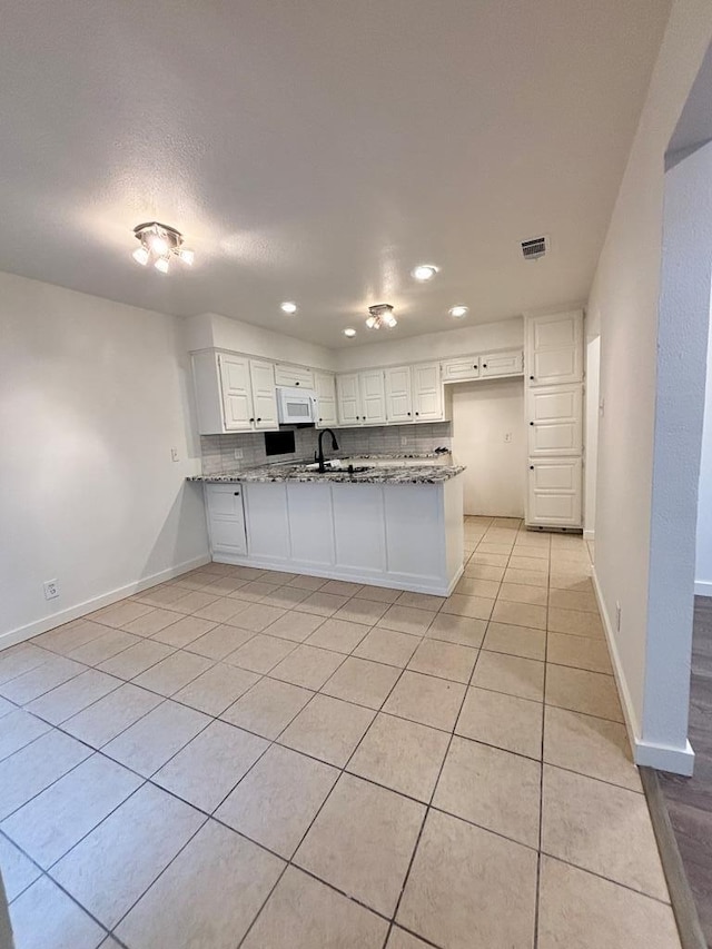 kitchen featuring white microwave, decorative backsplash, stone counters, and a peninsula