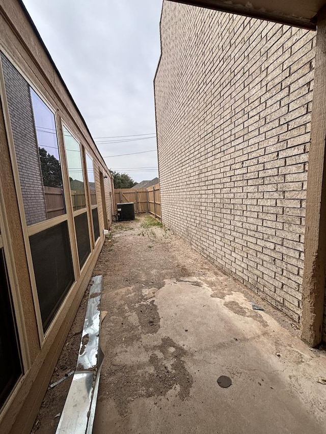 view of property exterior with brick siding, central AC unit, and fence