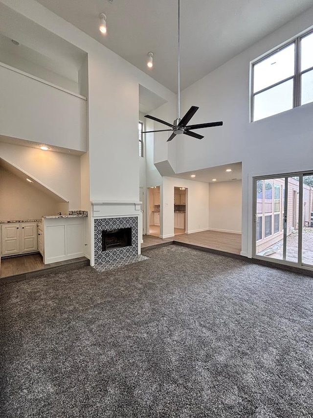 unfurnished living room with a ceiling fan, a tiled fireplace, a high ceiling, and carpet