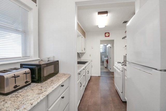 601 E 1st St, Coleman, TX 76834 - kitchen with white appliances, white cabinetry, dark wood-style floors, and light stone counters