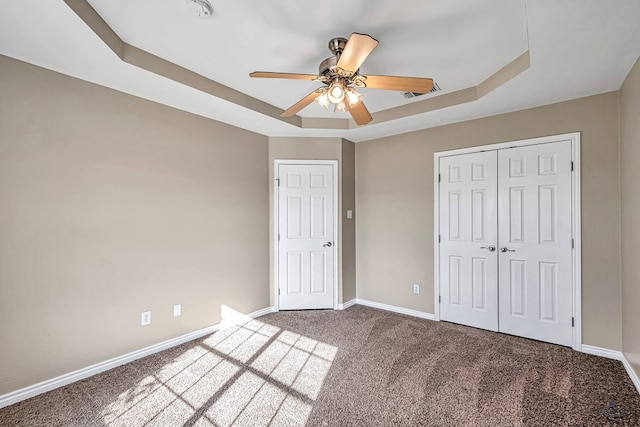 unfurnished bedroom featuring ceiling fan, a tray ceiling, carpet floors, and a closet