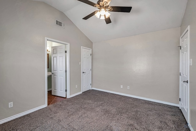 unfurnished bedroom with ceiling fan, ensuite bathroom, vaulted ceiling, and dark colored carpet