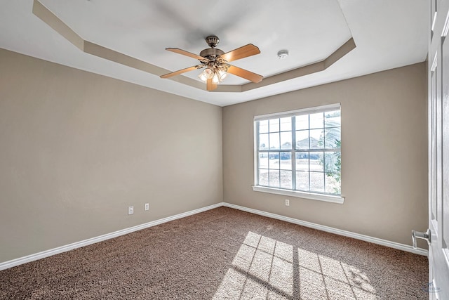 spare room with a tray ceiling, ceiling fan, and carpet