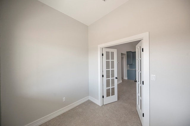 carpeted spare room with french doors and vaulted ceiling