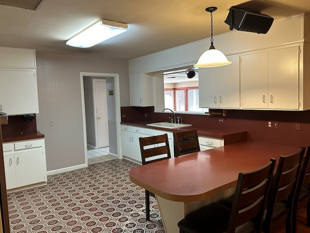 kitchen featuring kitchen peninsula, white cabinetry, sink, and hanging light fixtures